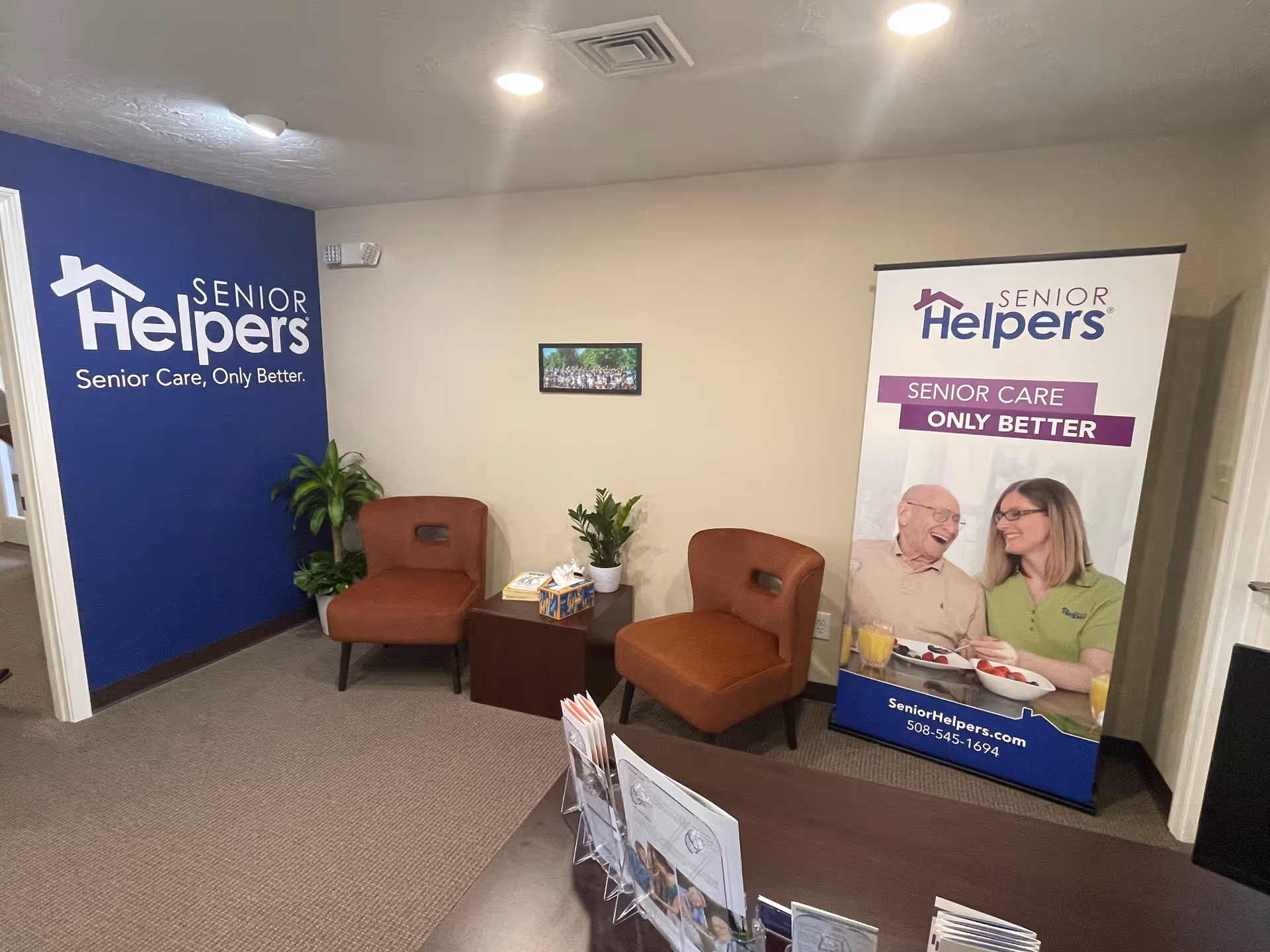 Reception area with blue wall featuring Senior Helpers logo and two orange chairs.