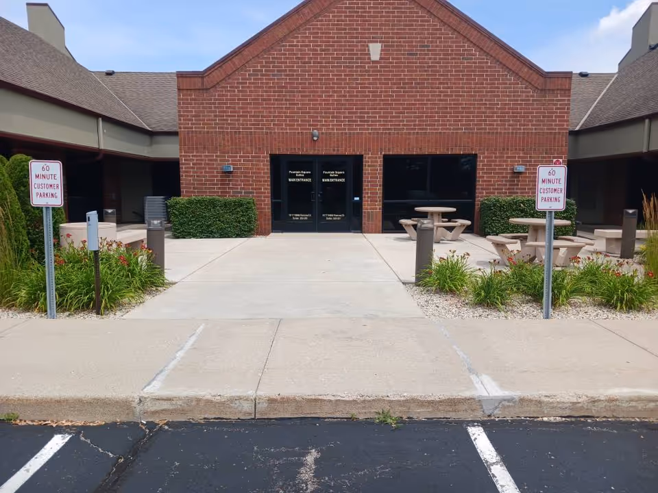 Exterior entrance of a brick senior living facility with outdoor picnic tables.