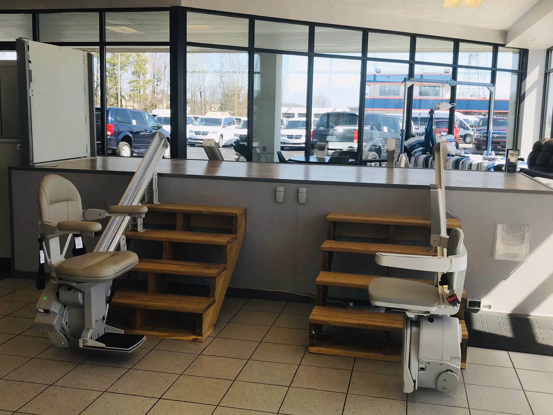 Indoor MobilityWorks showroom with two stair lift chairs and wooden steps near large windows.
