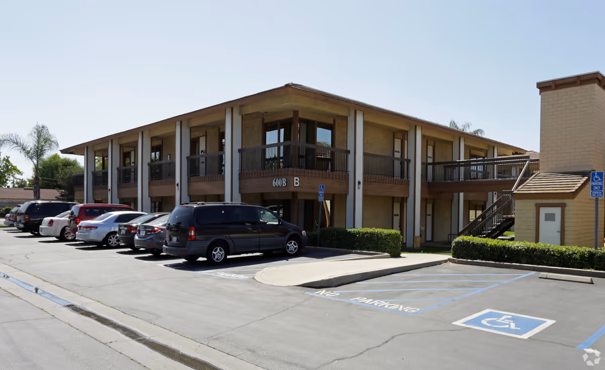 Exterior view of a two-story senior care building with parked cars in front.