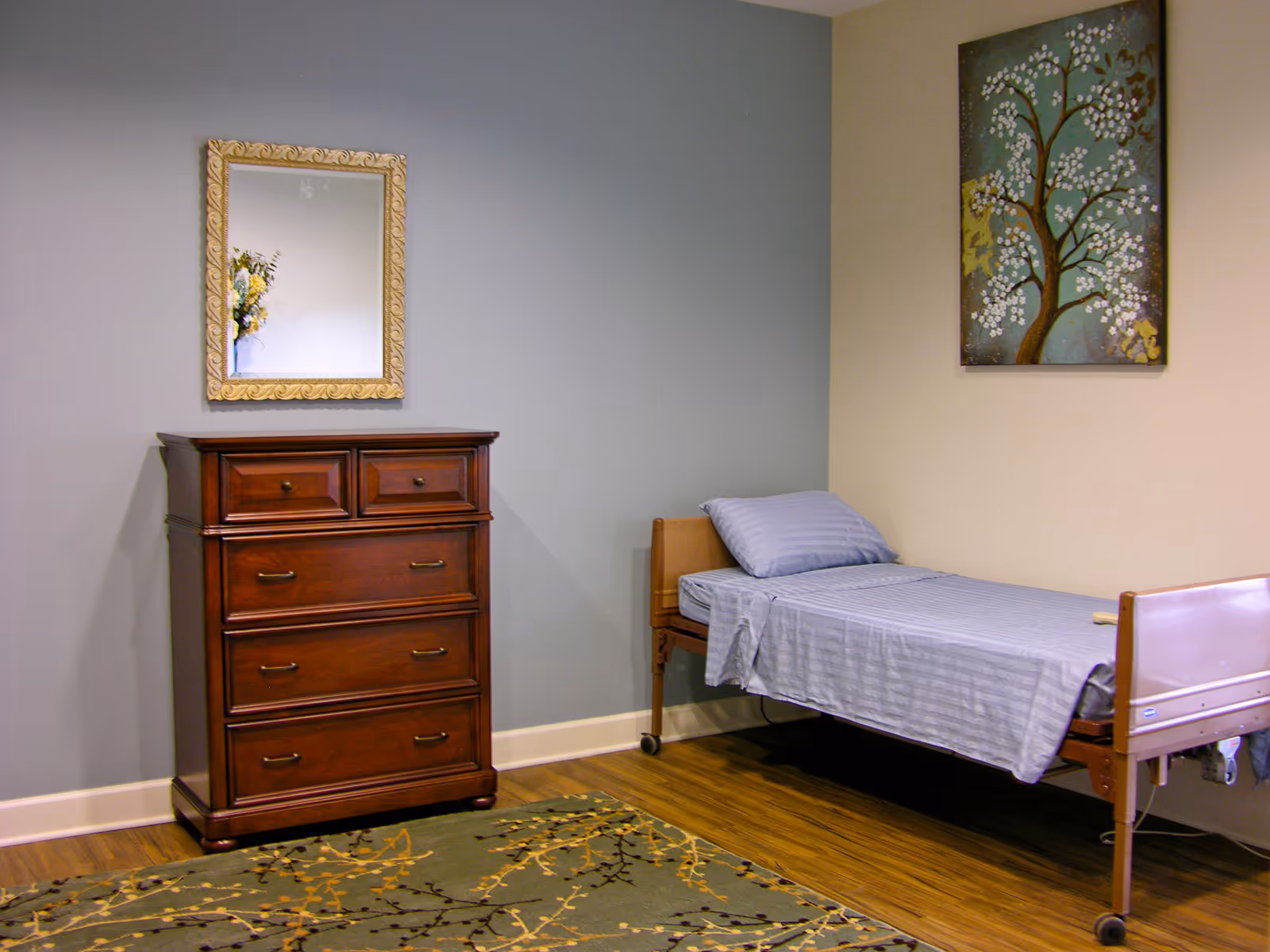 A bedroom in a senior facility with a wooden dresser, single bed, and wall art.