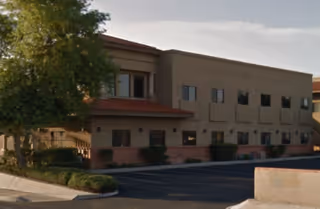 Front exterior of a beige, two-story senior living facility with landscaping and parking.