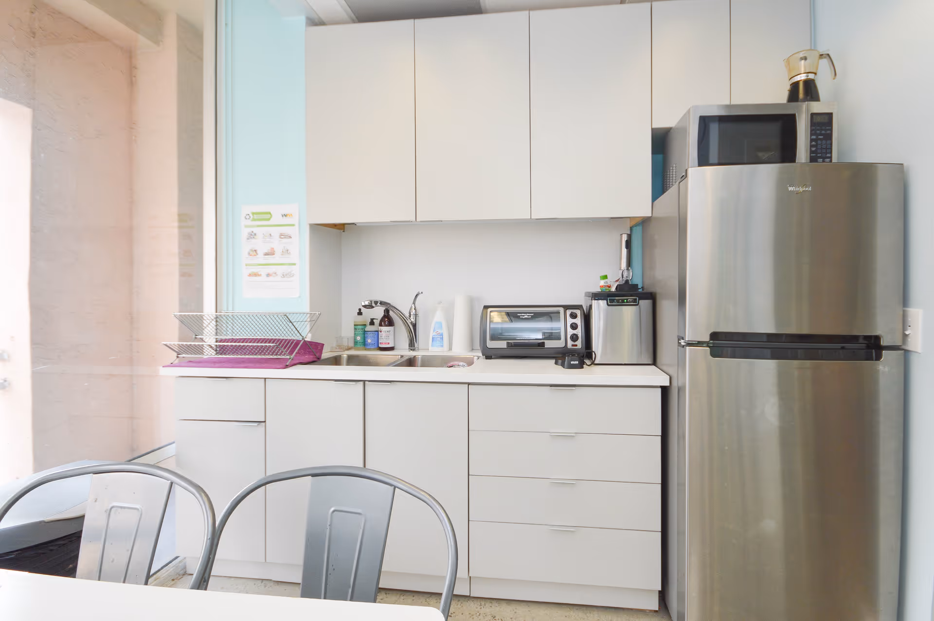 Small white kitchen with sink, fridge, microwave, toaster, and dish rack.