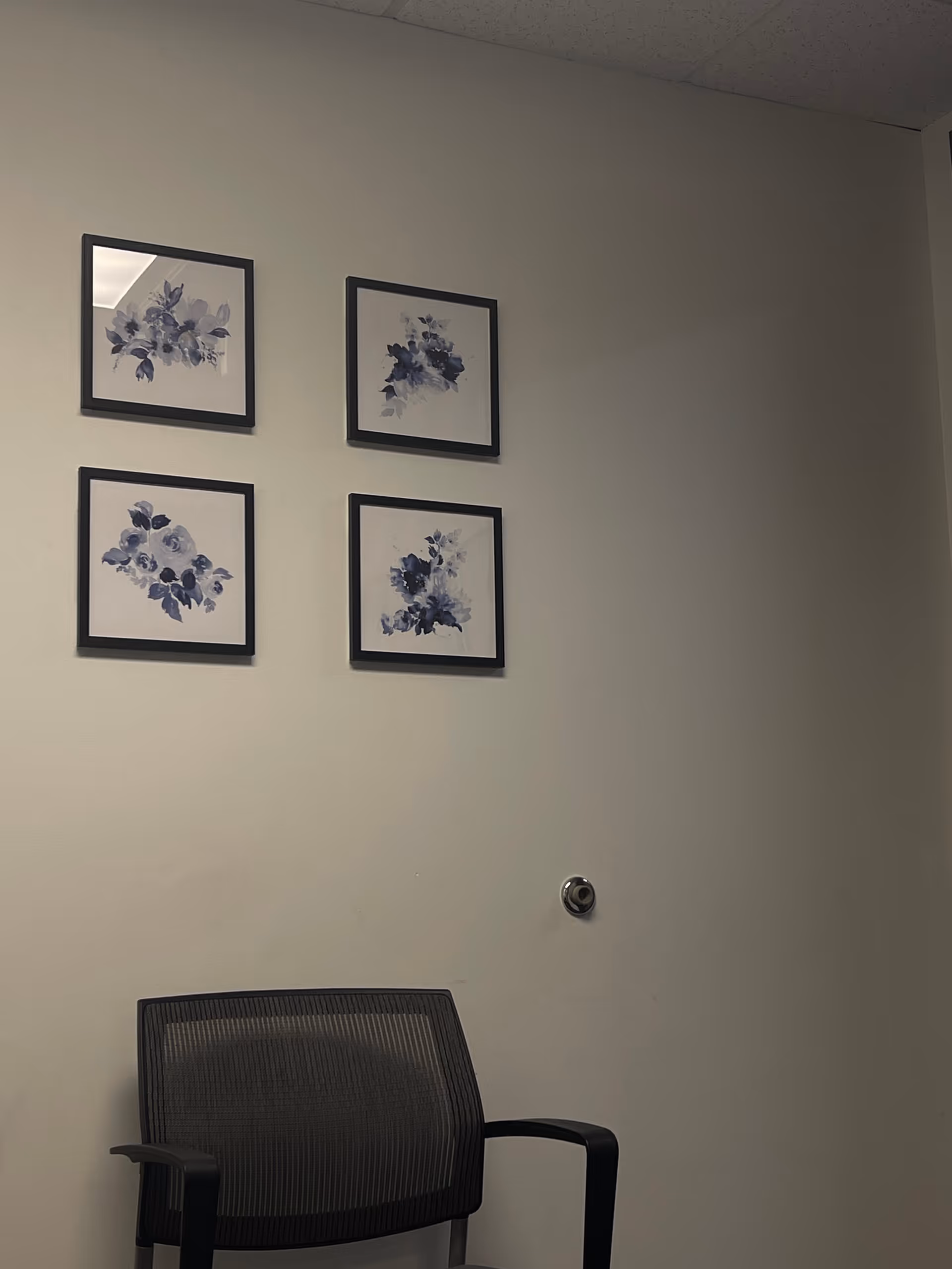 Interior corner with four framed floral prints and a black chair.