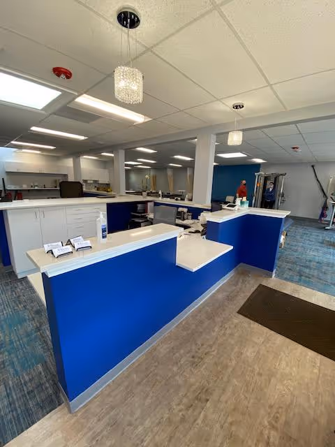 Blue reception desk in a rehab clinic lobby with desks and equipment visible.