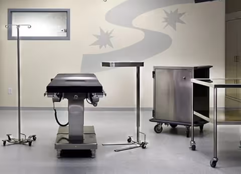 An empty surgical room with an operating table, IV stand, and medical carts.