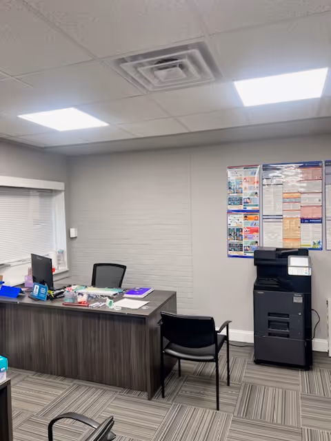 Office reception area with desk, chairs, copier, bulletin board, and window blinds.