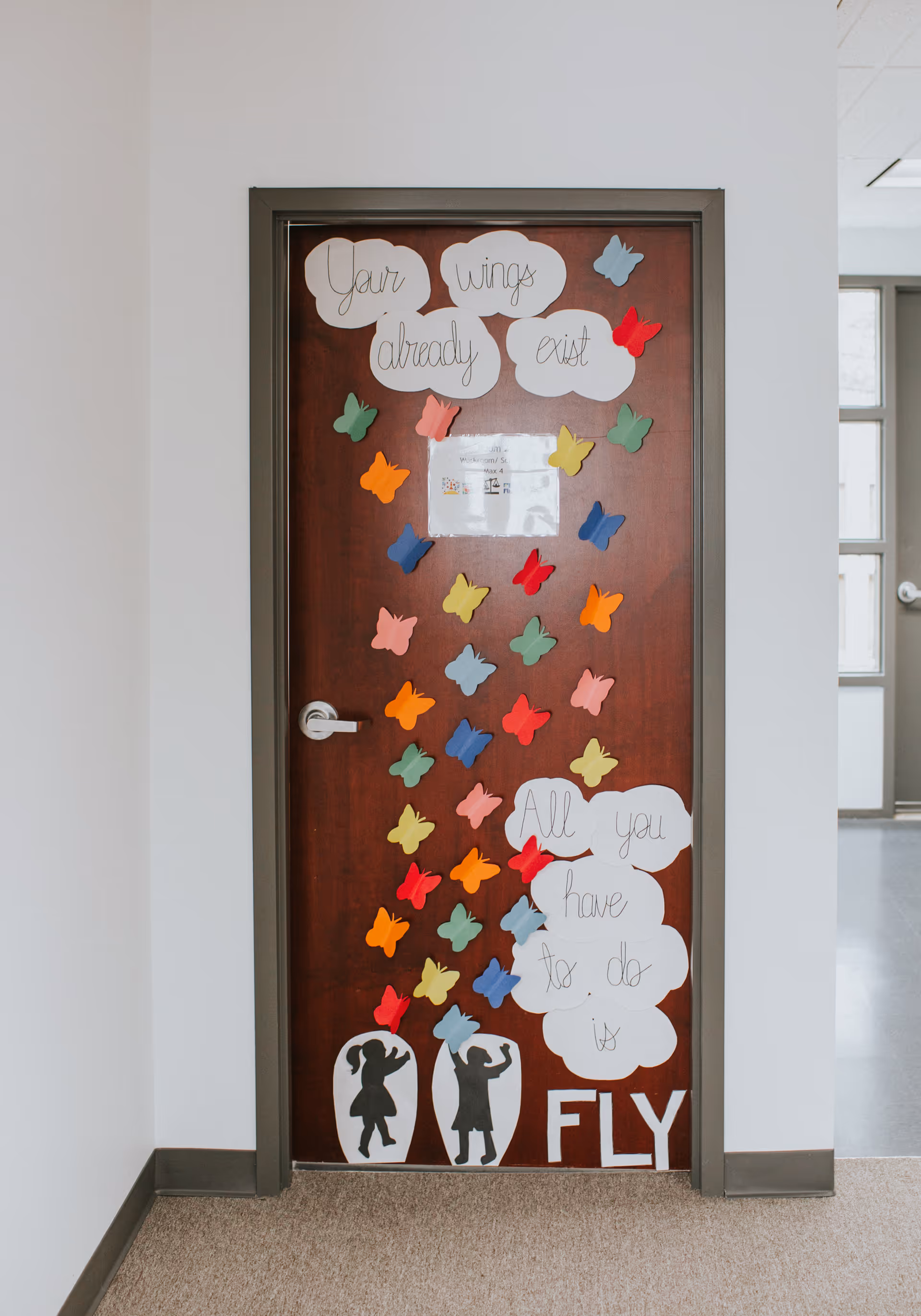 Wooden door in a hallway decorated with colorful butterfly shapes and quotes.