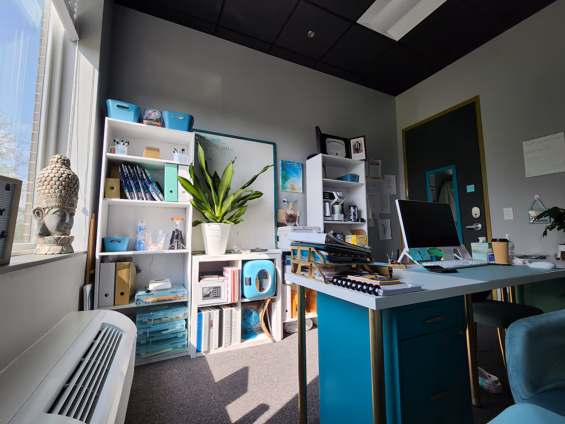Office workspace inside a senior living facility with desk, shelves, plant, and supplies.