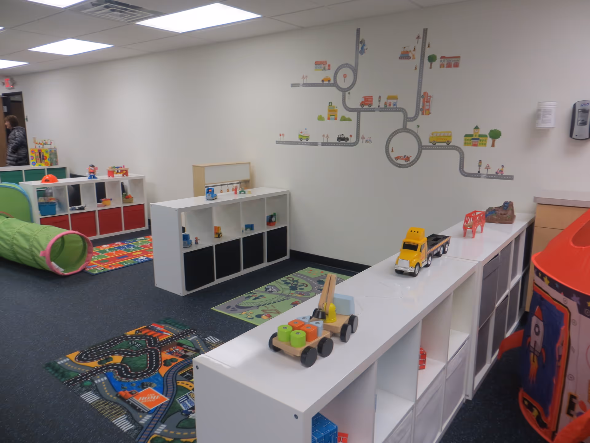 Bright children's play area with toy shelves, road mural, and colorful carpet mats.