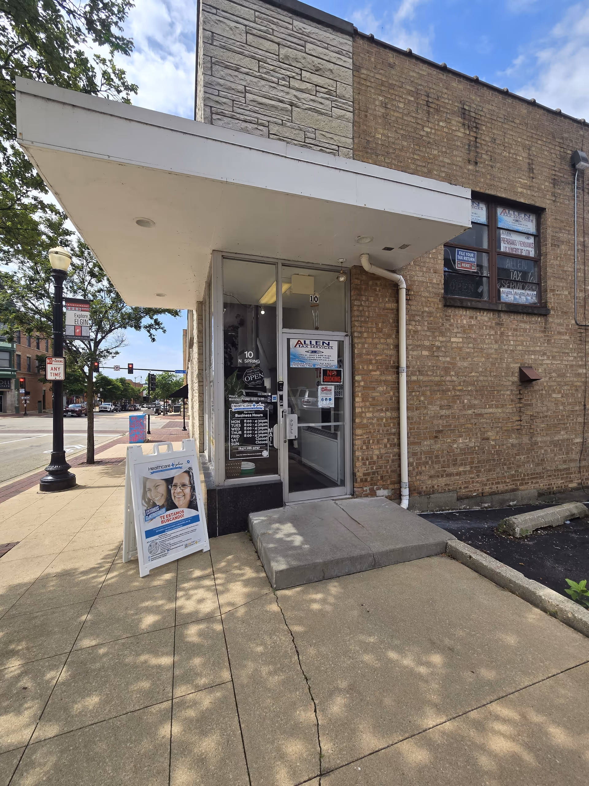 Exterior view of a brick storefront with glass door, sidewalk, and signboard.