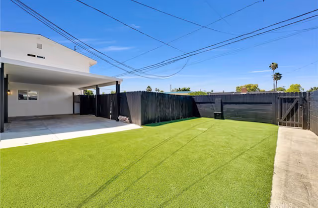 Outdoor courtyard with artificial turf, a covered patio, and dark wooden fencing.