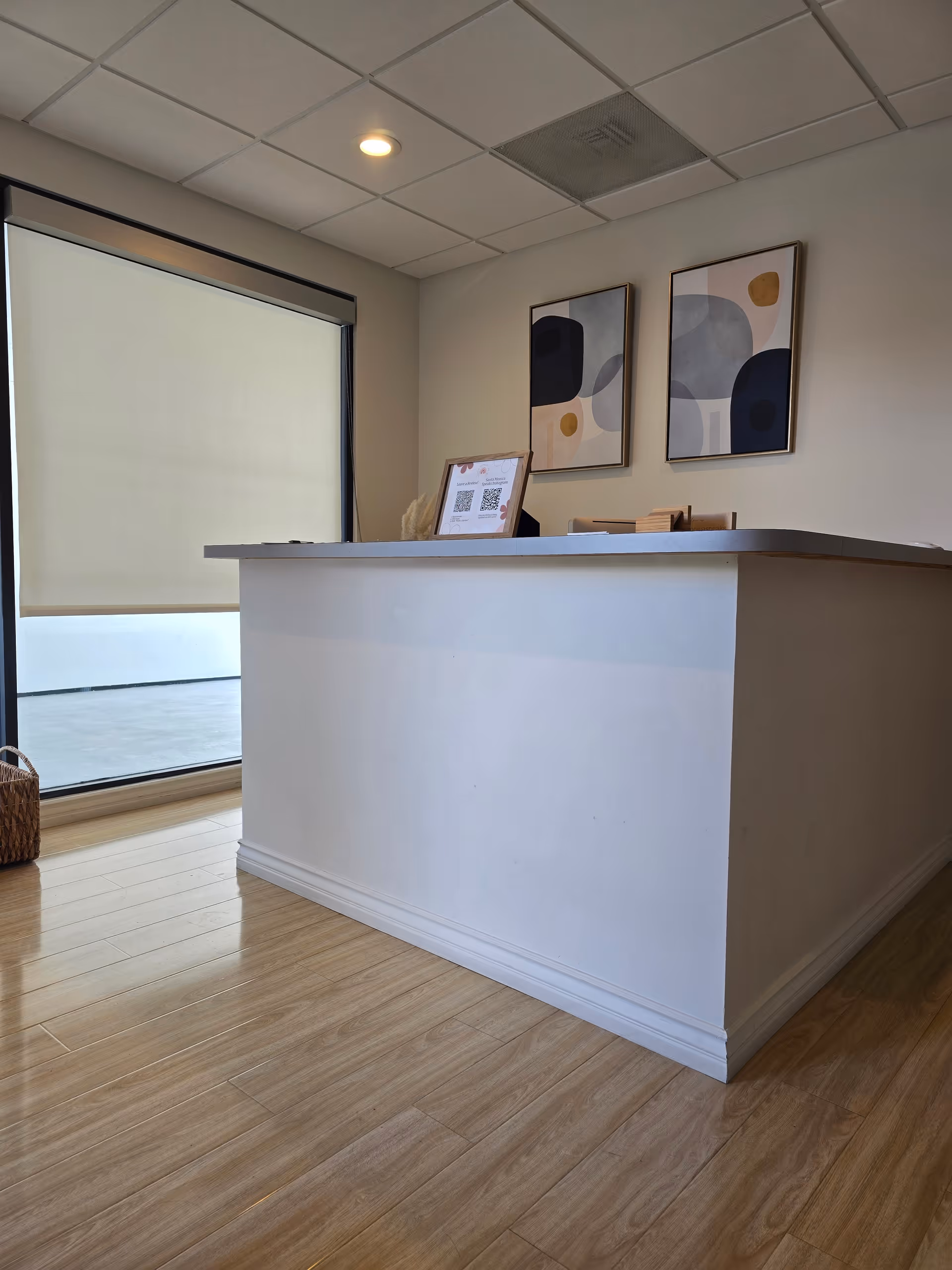 Reception desk in a modern interior with abstract wall art, large window, and wooden floor.