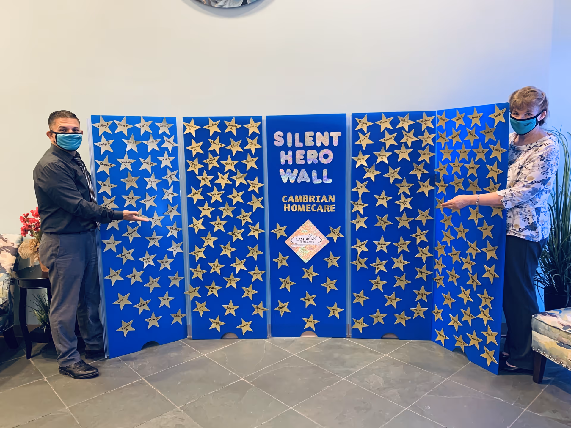 Two masked people stand beside a blue Silent Hero Wall display covered in stars.