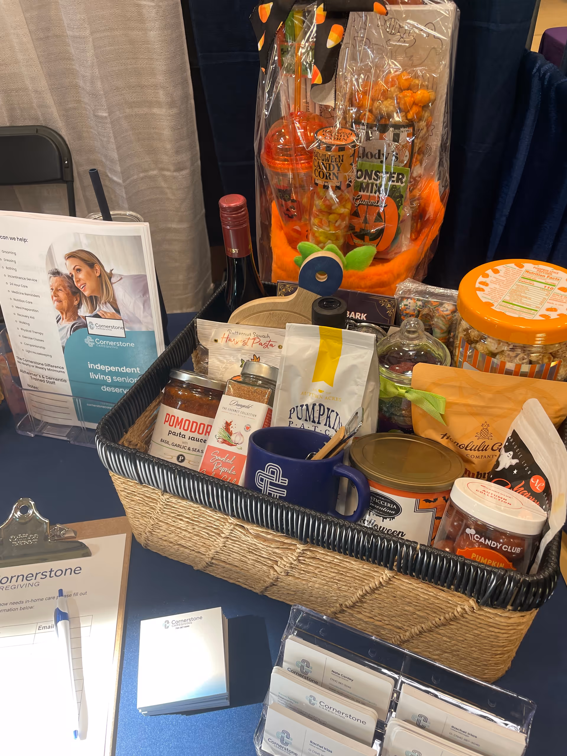 Basket filled with snacks, pumpkins, and informational materials at a Cornerstone Caregiving booth.