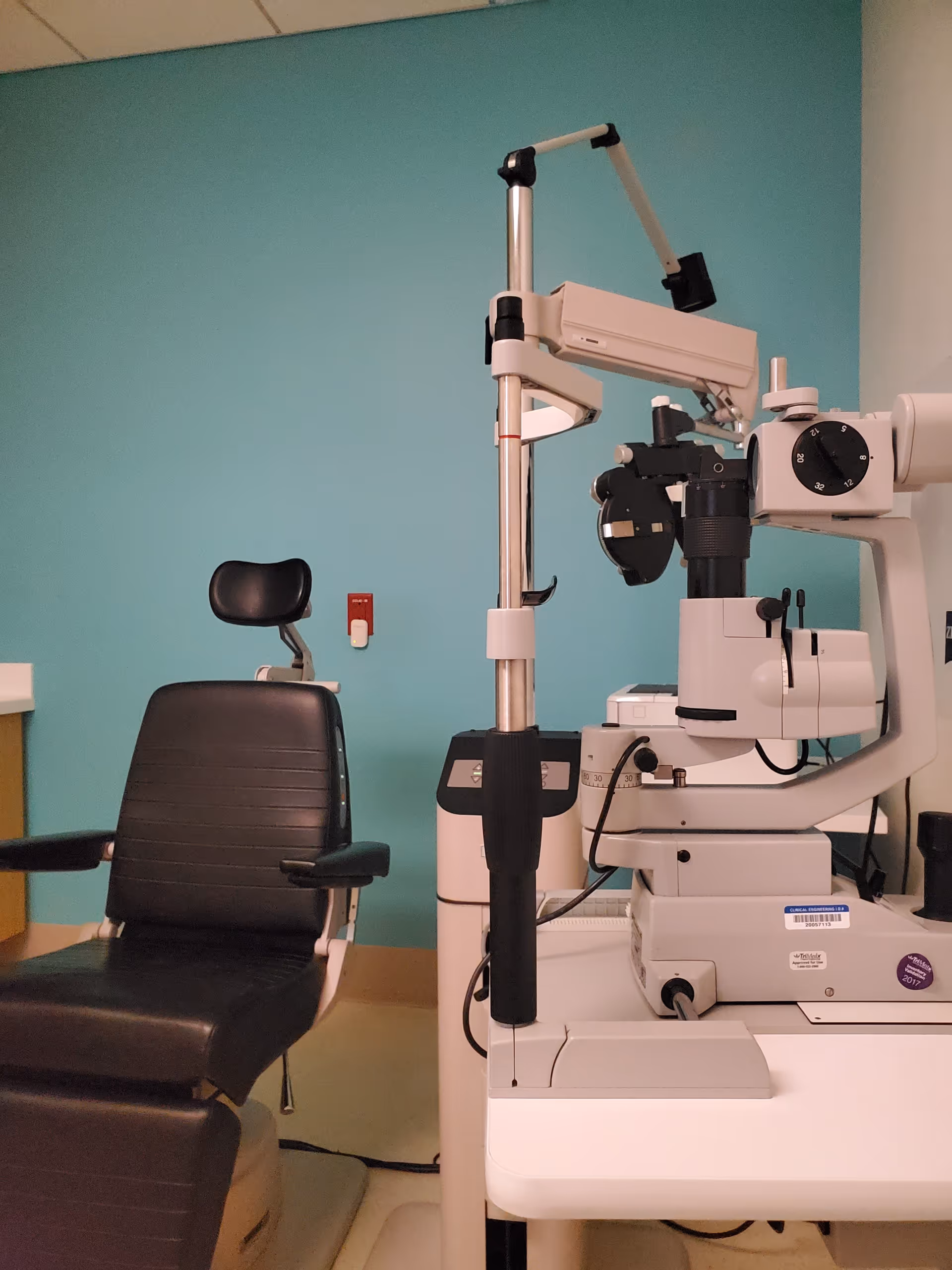 Clinic room with ophthalmology equipment, chair, and teal wall behind.
