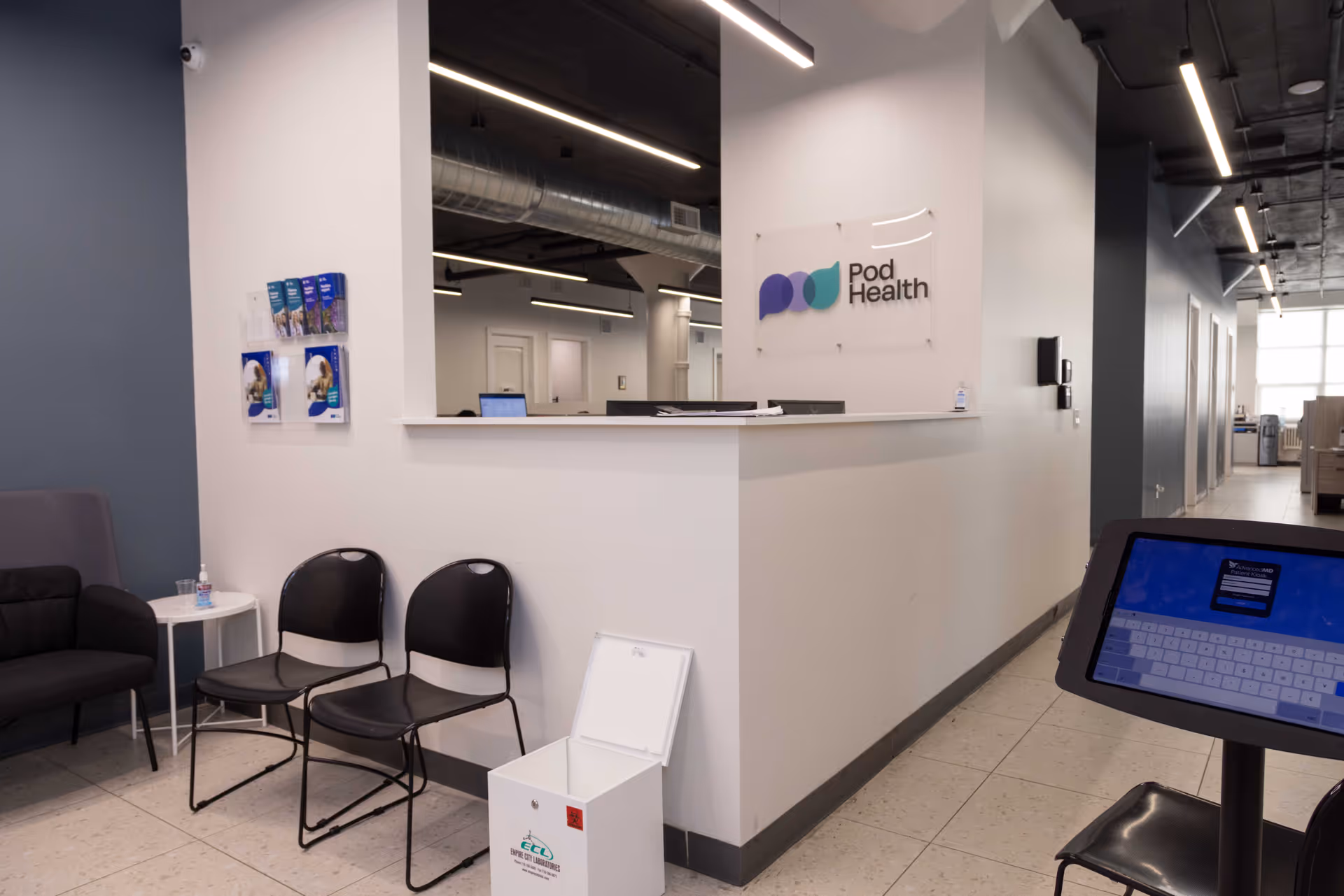 Reception area with Pod Health sign, white counter, and empty chairs.