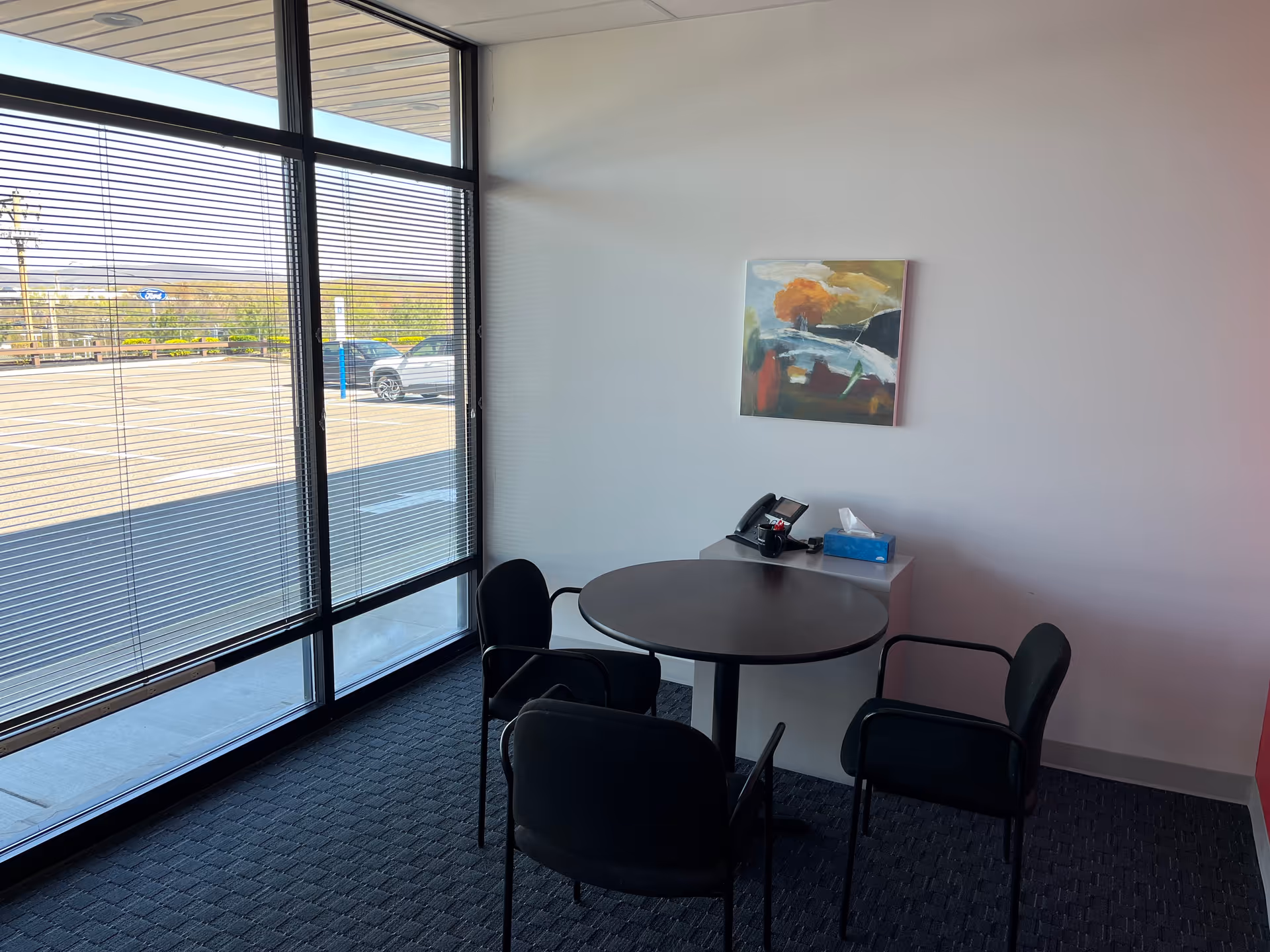 Small interior seating area with round table, four chairs, large windows, and wall painting.
