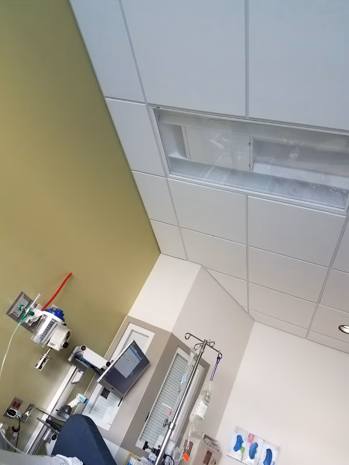 Medical equipment and IV stand in a hospital room with tiled ceiling.
