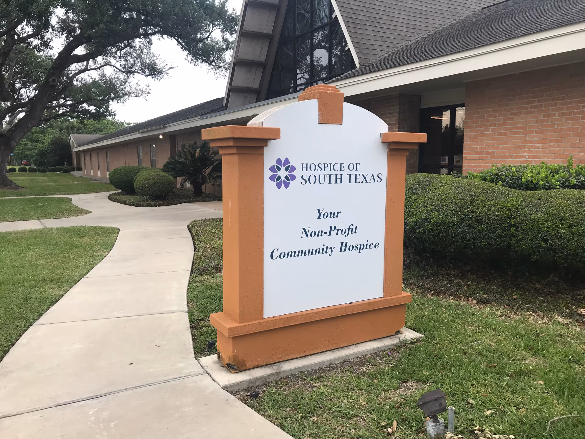 Exterior view of Hospice of South Texas sign beside a curved sidewalk.