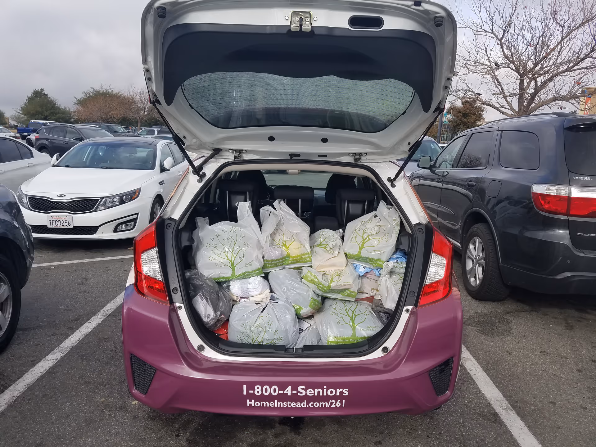 Open trunk of a purple hatchback filled with donation bags in a parking lot.