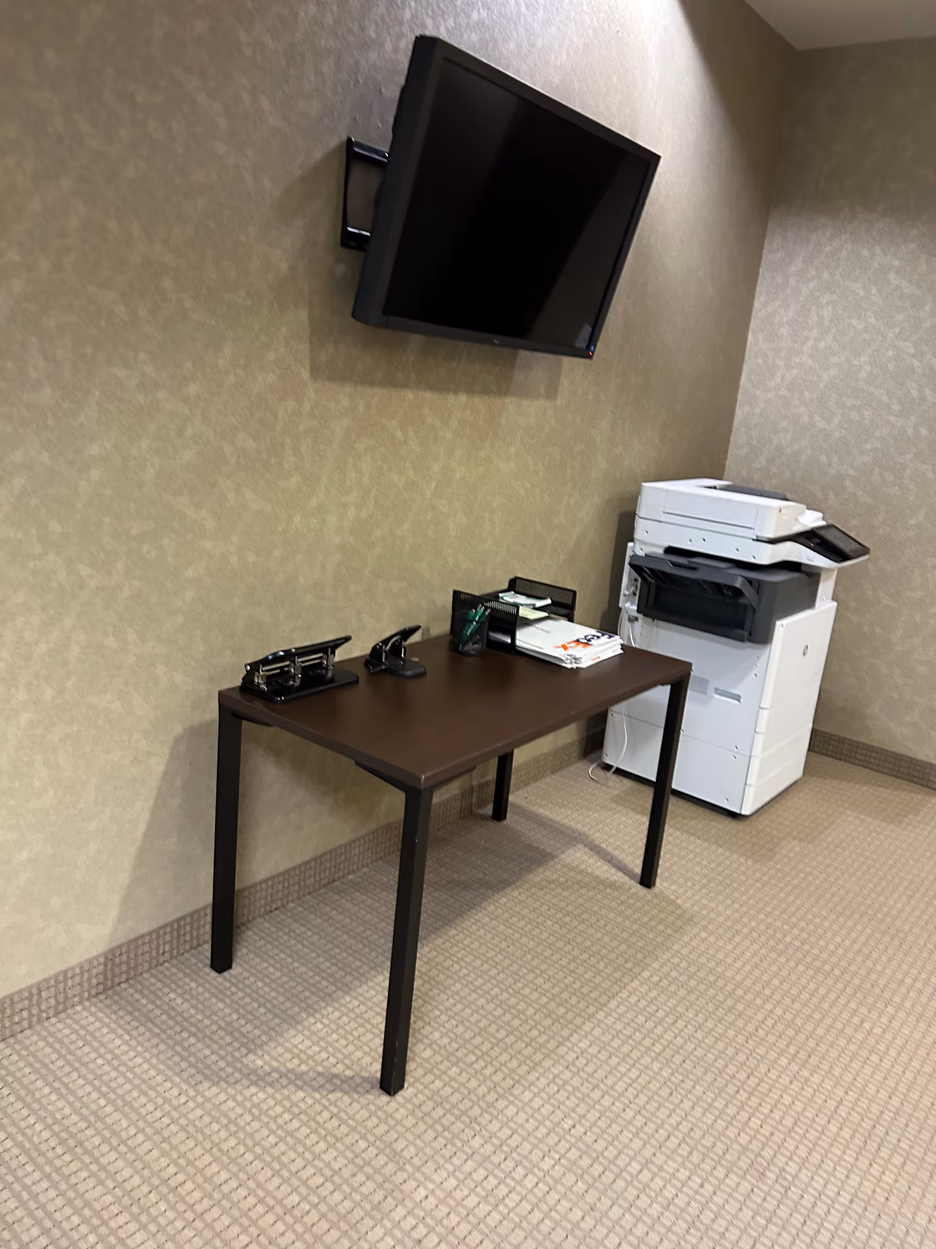 A small interior office corner featuring a wall-mounted TV, desk, and a copier.