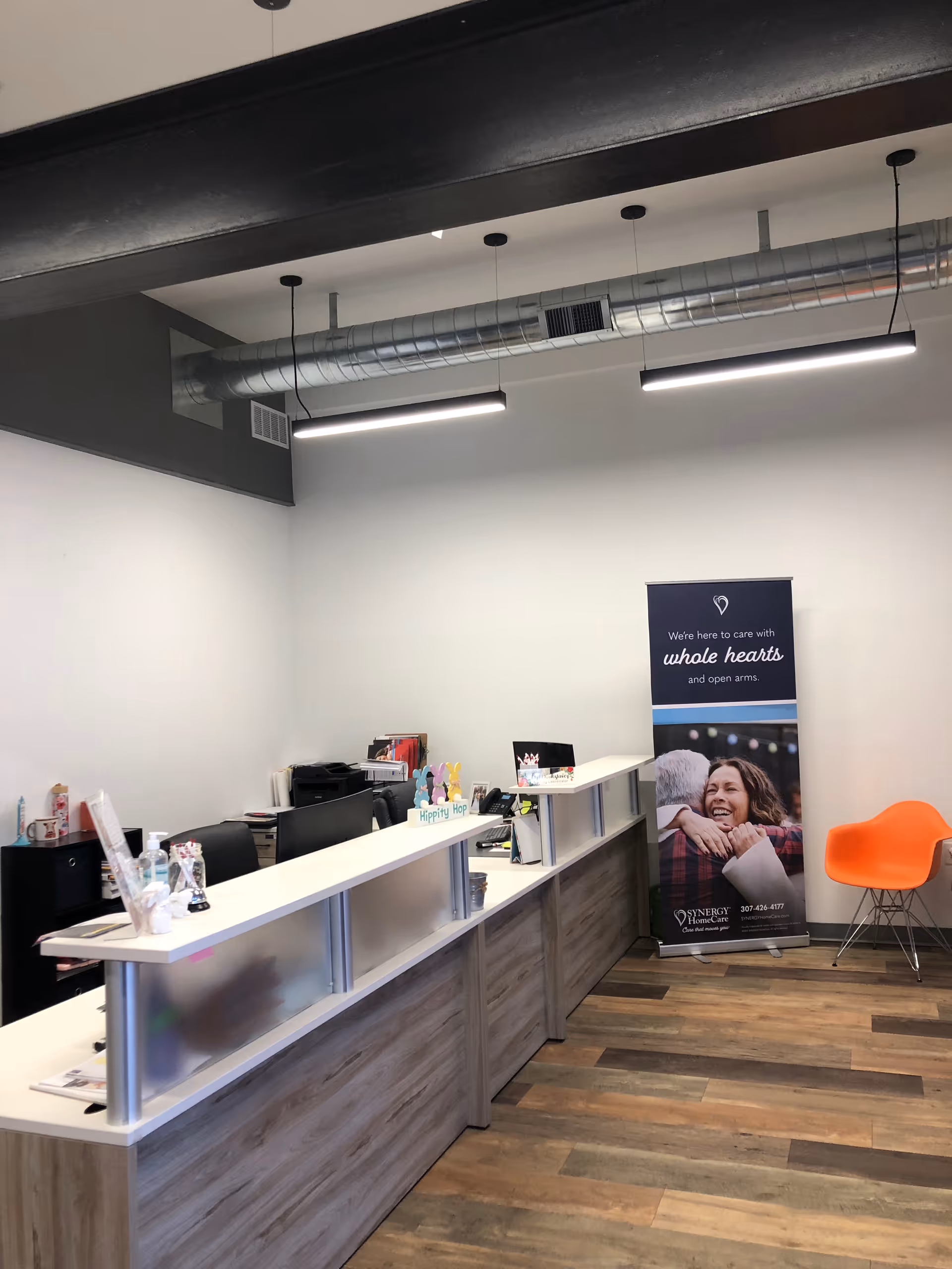 Reception area with a long white counter, banner, and orange chair in a modern interior.