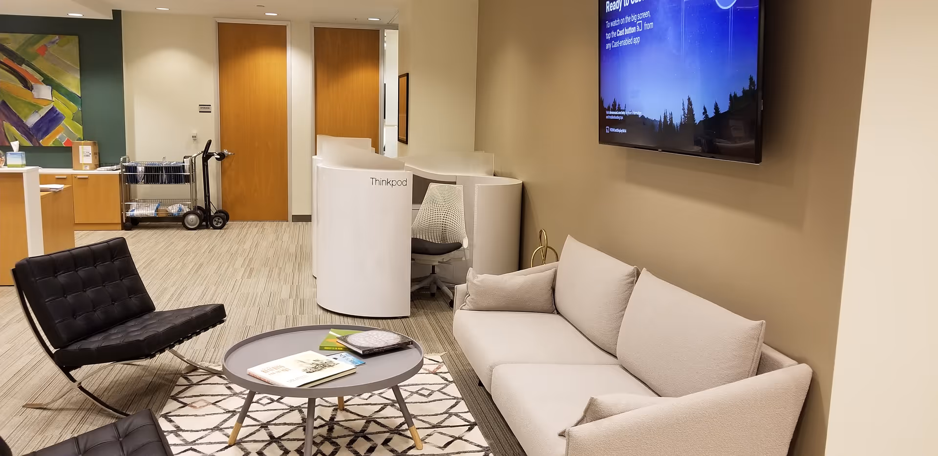 Modern facility lounge with a sofa, black lounge chairs, round coffee table, and wall mounted TV.