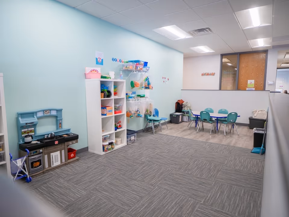 Interior play area with toy shelves, kitchen set, and small tables in pastel teal walls.