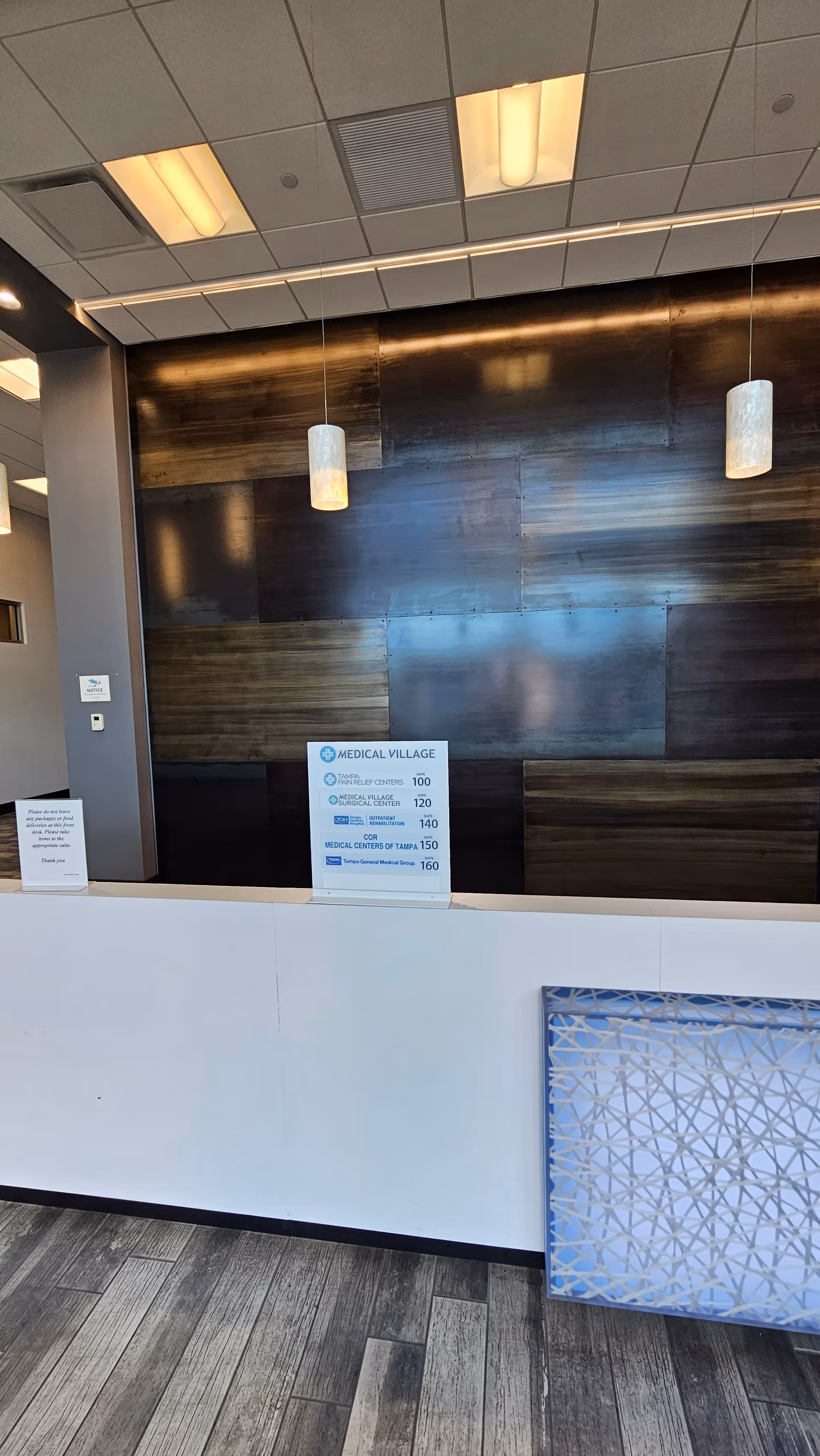 Reception area with white counter and dark wood paneled wall, hanging lights.