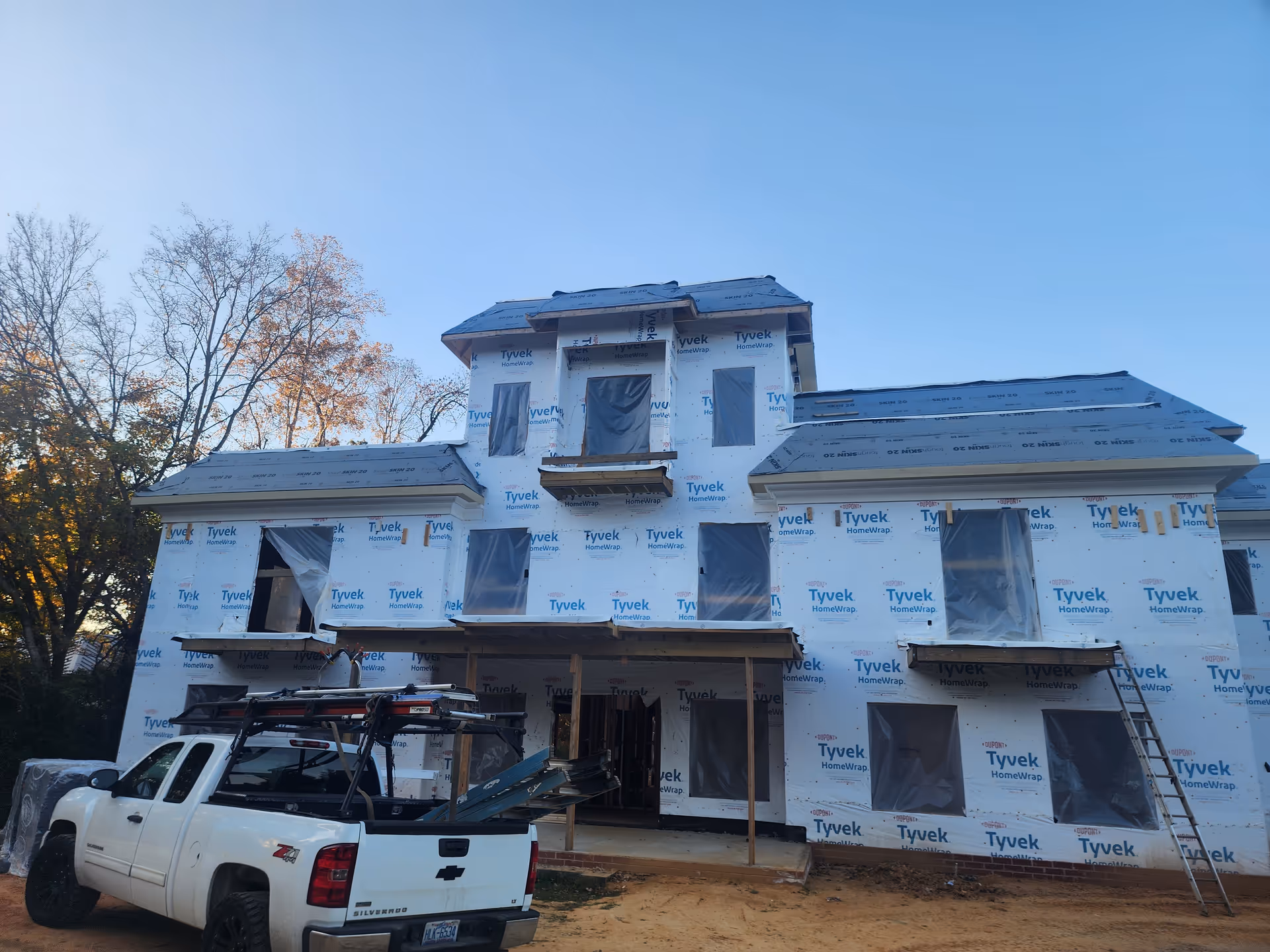 A two-story house under construction wrapped in Tyvek with a white pickup truck nearby.