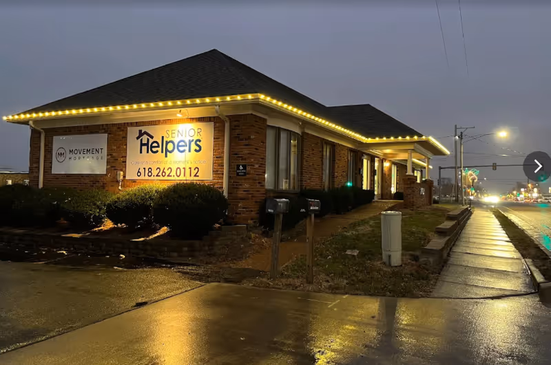 Exterior brick building with illuminated roofline lights and Senior Helpers sign at dusk.
