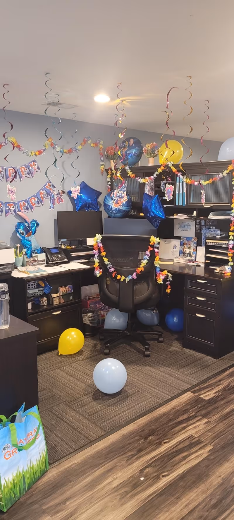 Festive office desk setup with birthday banner, balloons, and streamers in a reception area.