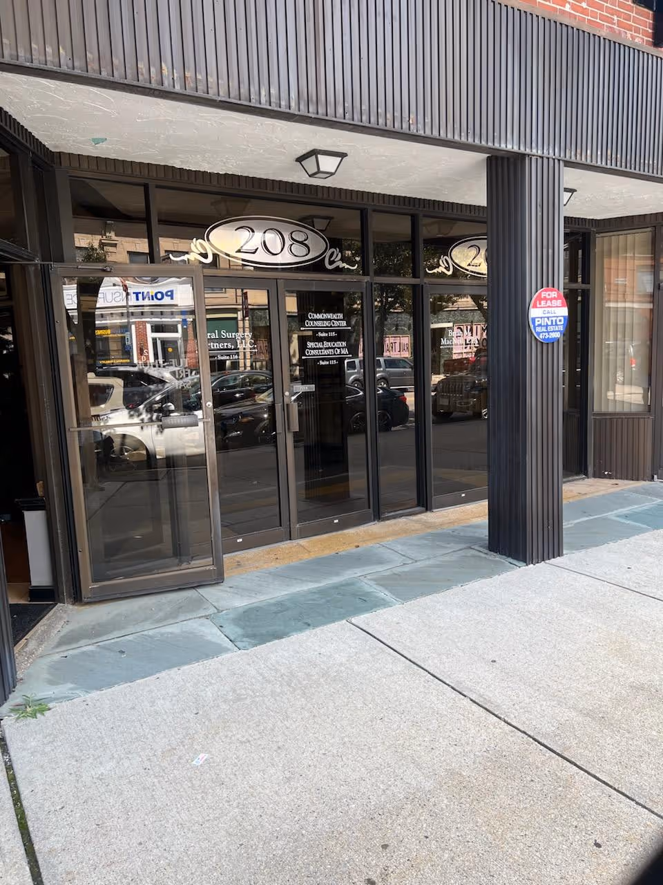 Glass storefront entrance with large doors, black frames, and reflections of passing cars outside.