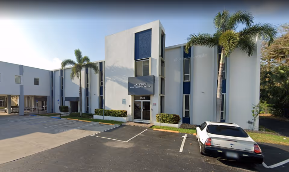 Exterior view of a modern senior care facility with palm trees and parking.