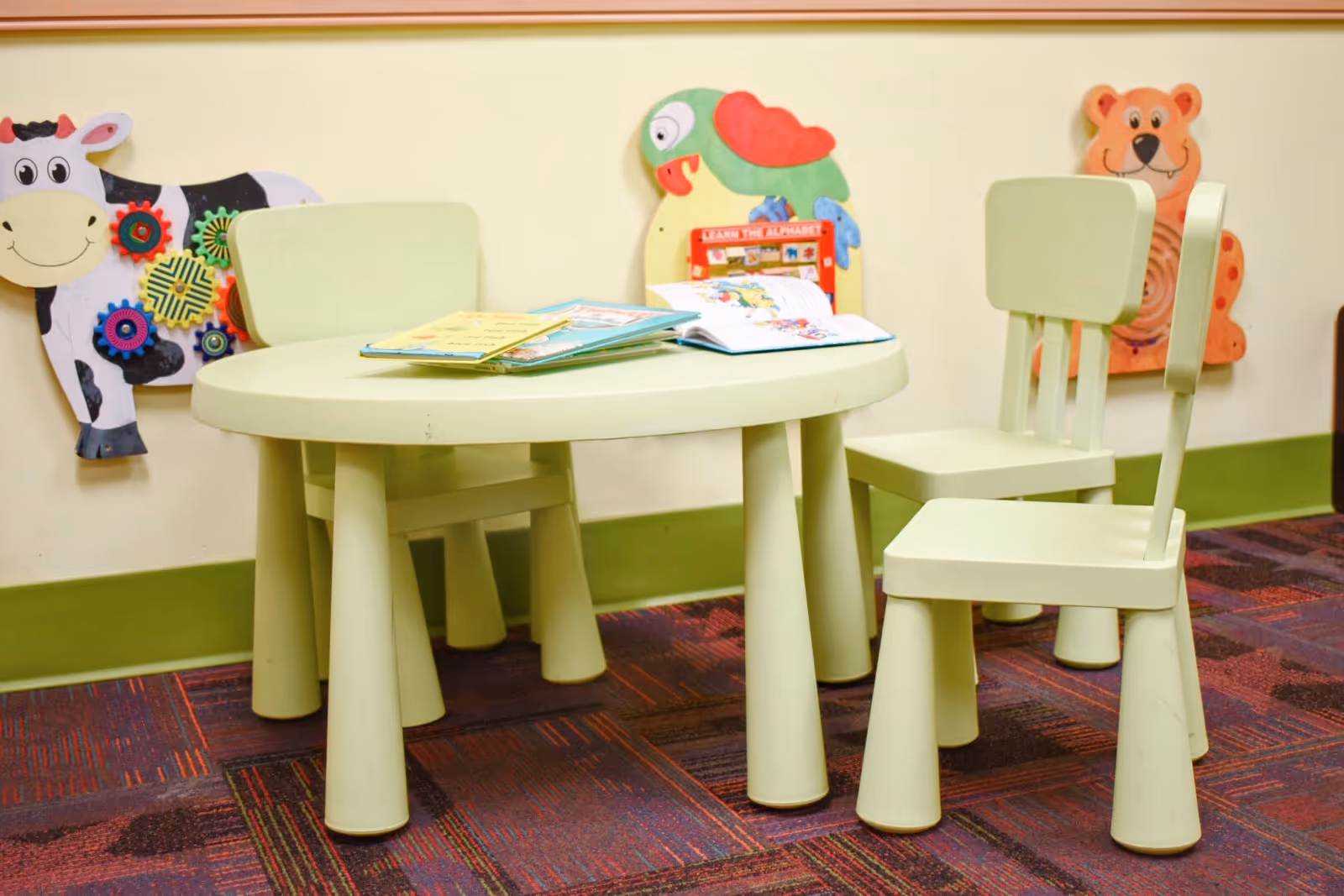 Pale green round table with matching chairs in a colorful children's play area.