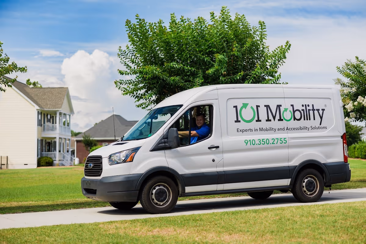 White 101 Mobility van with logo parked on a suburban street; driver visible.