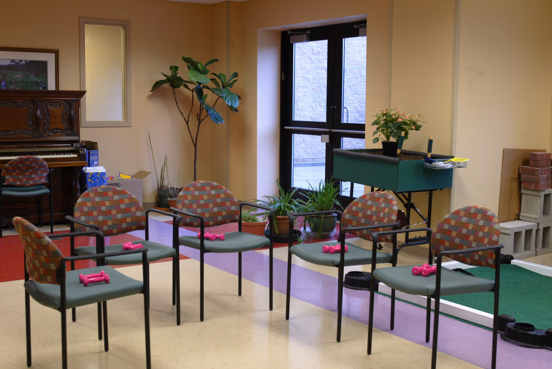 Chairs arranged in a circle with pink dumbbells in a senior living activity room.