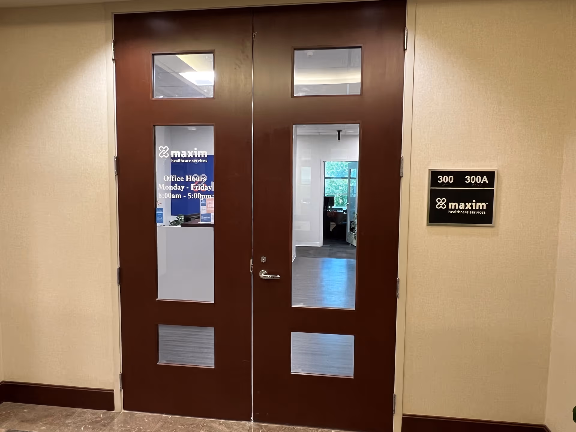 Double brown doors with glass panels in a hallway beside a Maxim sign.