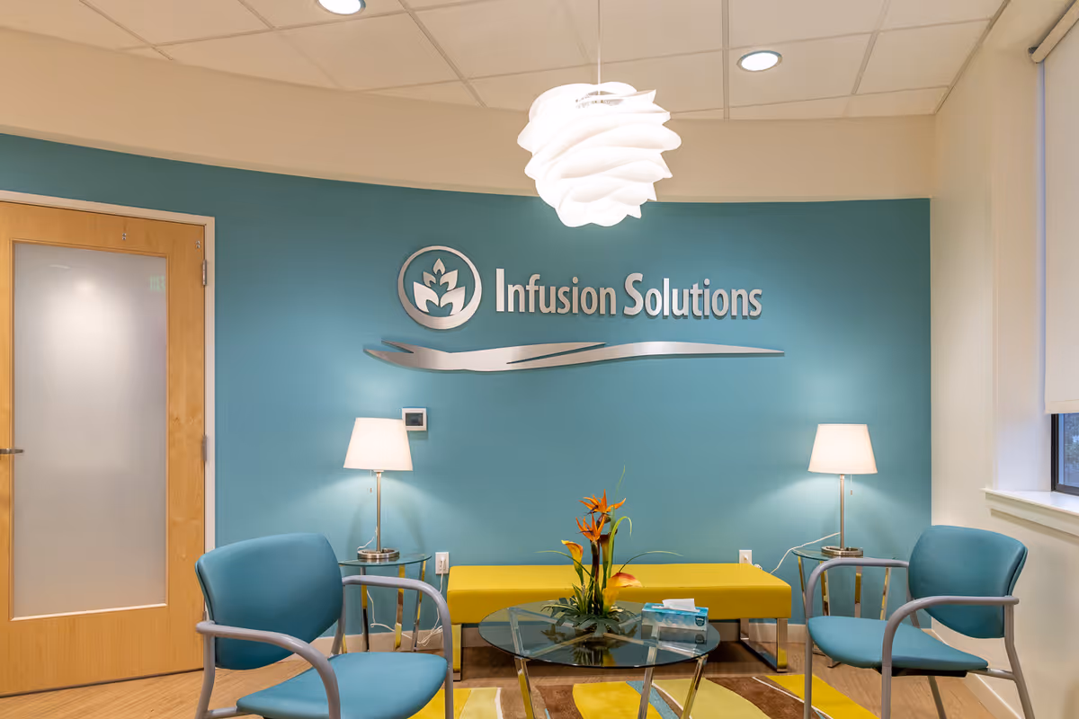 Infusion Solutions lobby with teal wall, logo, lamps, glass coffee table, and blue seating.