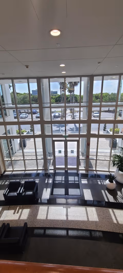 Bright lobby with floor-to-ceiling windows, glass doors, and black seating.