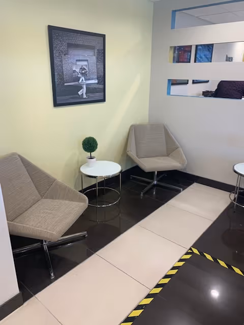 Modern waiting area with two gray chairs, small round tables, plant, and framed photo.