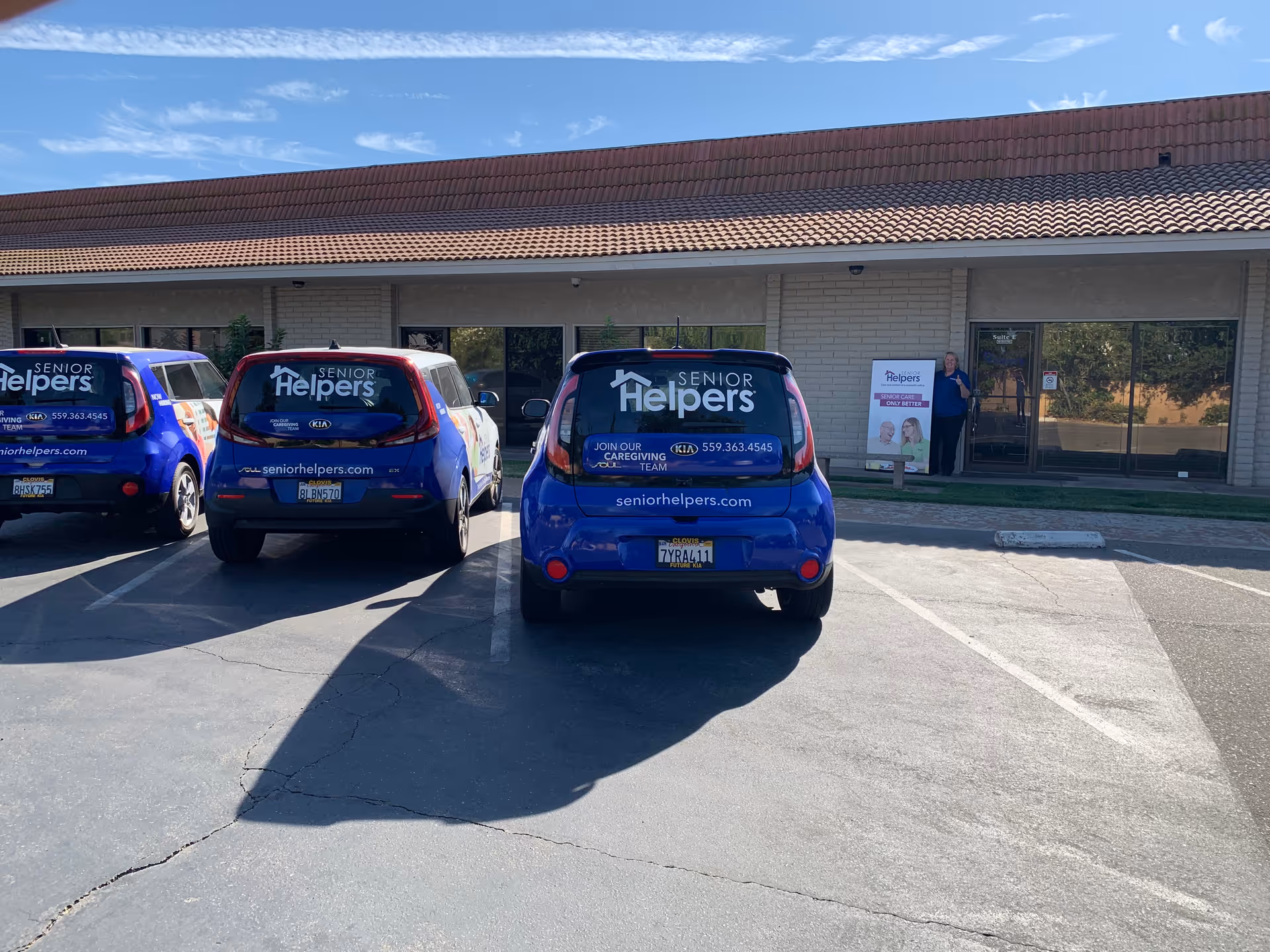 Blue Senior Helpers vans parked outside a single-story facility with glass doors and signage.