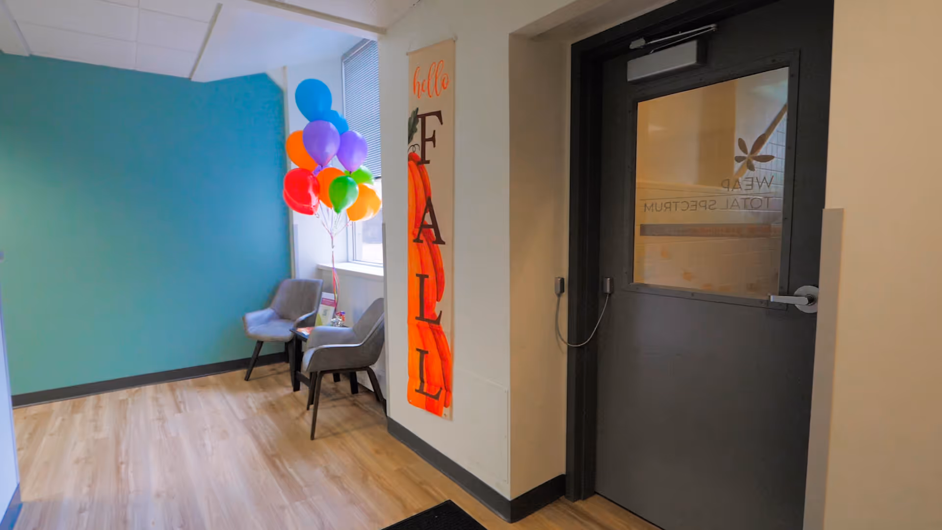 Waiting area in a facility hallway with teal wall, balloons, and two chairs.