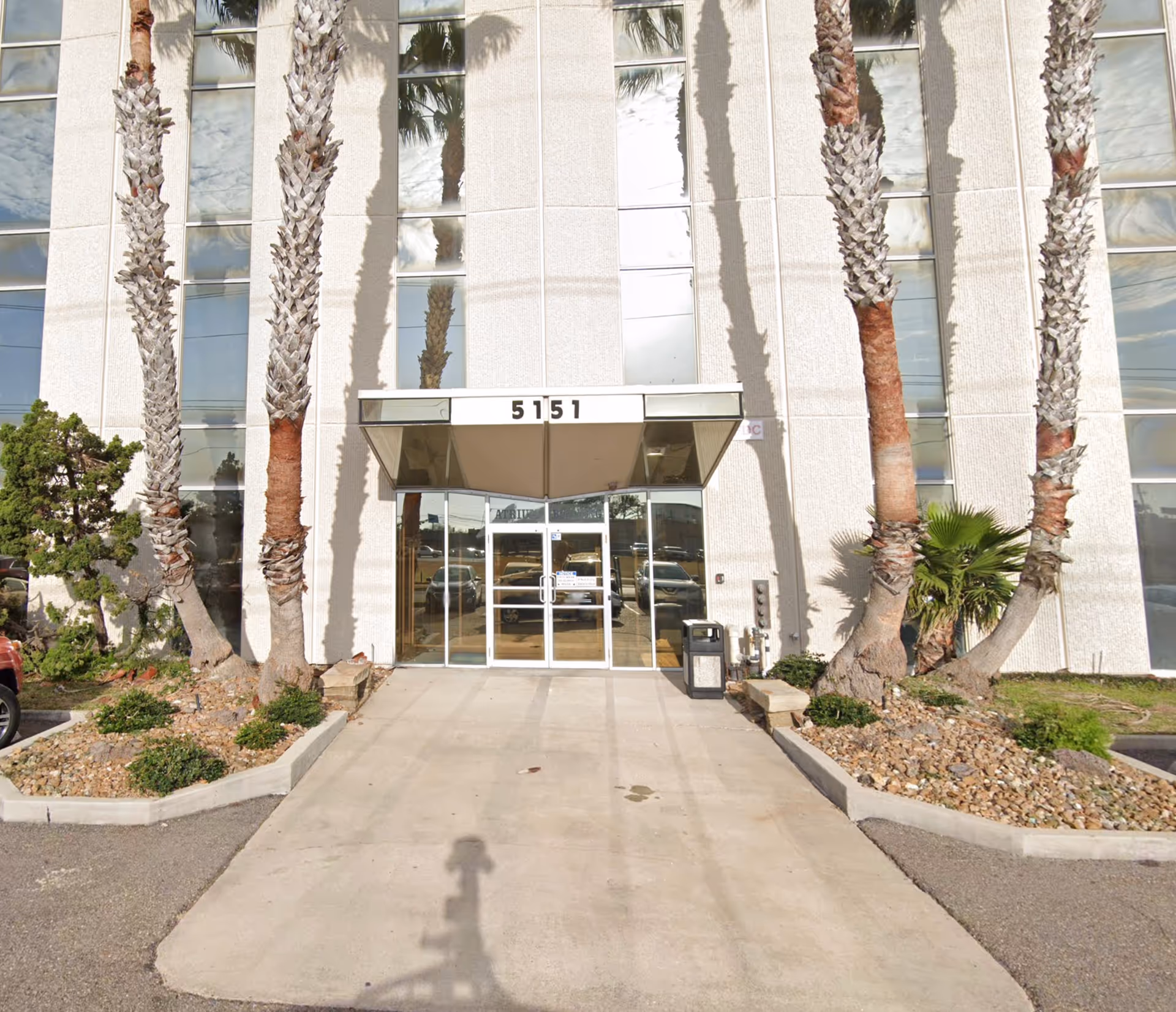 Front entrance of a building with glass doors and tall palm trees.