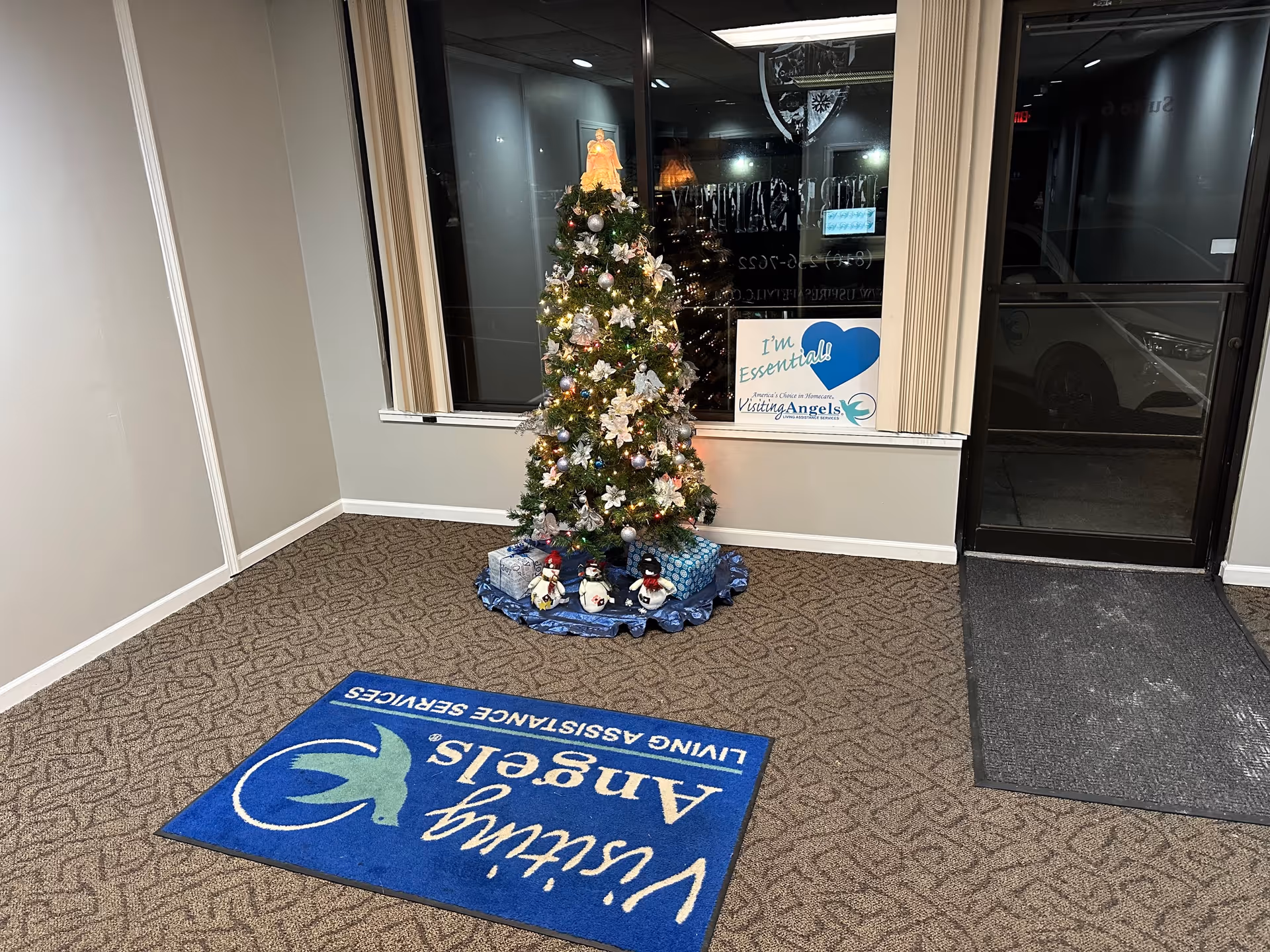 Inside a facility lobby, a decorated Christmas tree near a window and a blue mat.