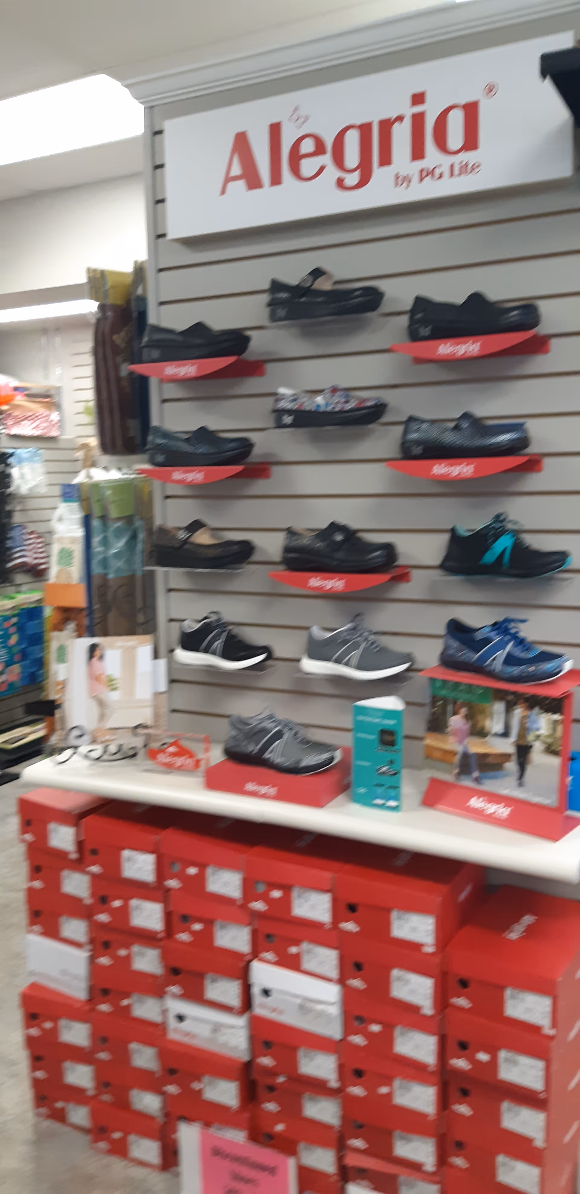 Shoe display wall featuring Alegria brand shoes and stacked red shoeboxes in a retail aisle.