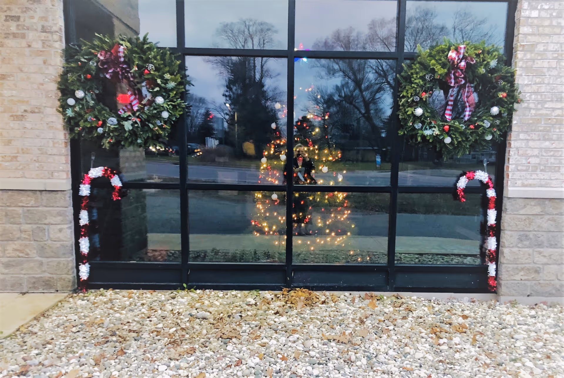 Decorated glass entrance with wreaths, a reflected Christmas tree, and holiday lights.
