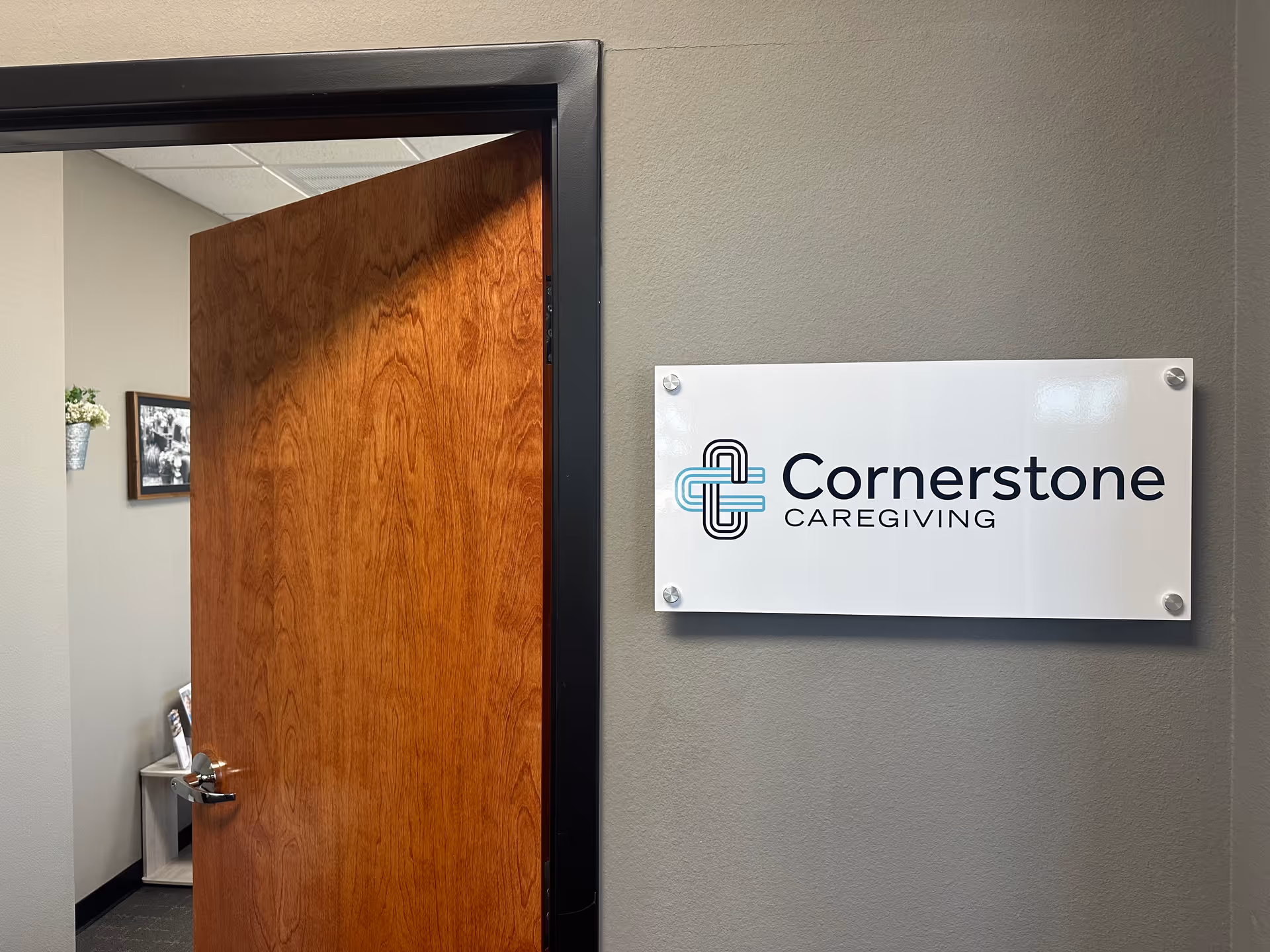 Open wooden door reveals gray interior walls and a Cornerstone Caregiving sign.