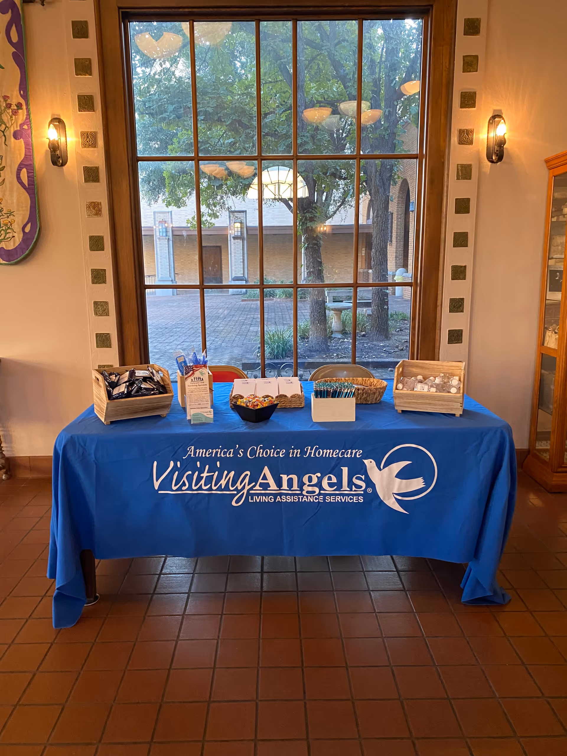 Blue Visiting Angels table with brochures inside a lobby, large window behind.